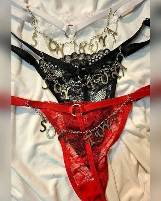 Tres colaless de encaje —blanco, negro y rojo— con letras metálicas colgando de una cadenita que arman la frase "Soy tuya".
