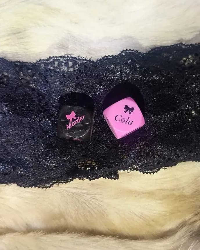 Los dos dados del juego, uno negro y uno rosa con palabras impresas, apoyados sobre el lazo de encaje negro que viene para los ojos.