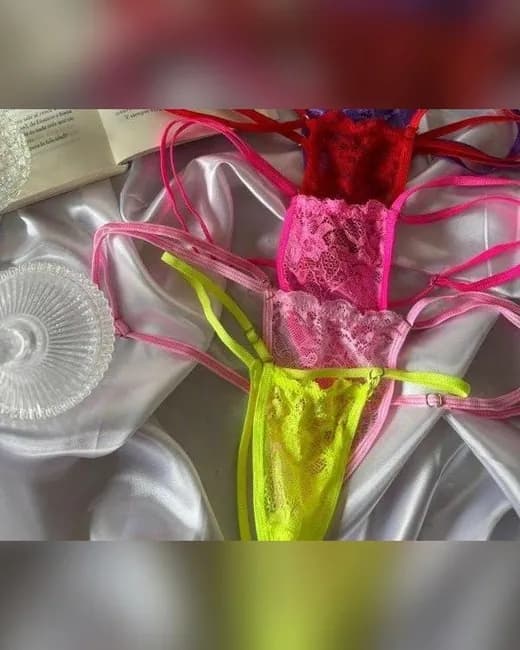 Varias colaless de encaje con triangulito y tiras finas, en rosa bebé, fucsia, rojo, violeta y amarillo flúor, sobre una tela de satén blanca.
