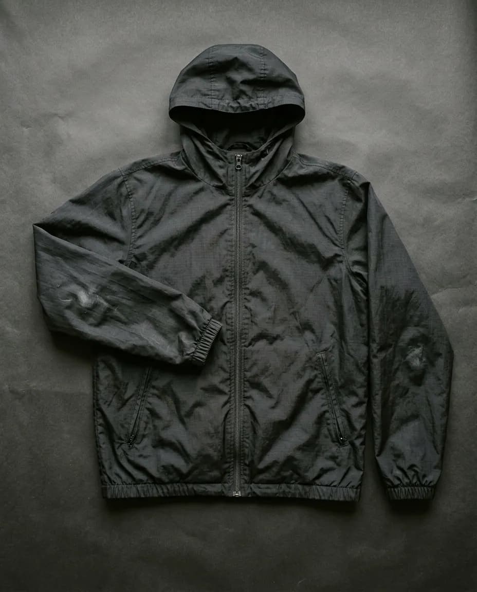 Campera rompeviento de nylon negro extendida sobre un fondo de papel oscuro