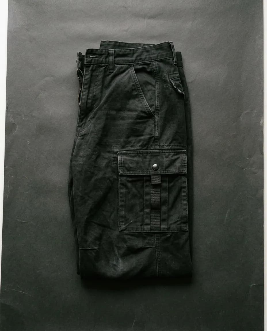 Pantalón cargo negro doblado sobre un fondo de papel oscuro, con el bolsillo lateral a la vista