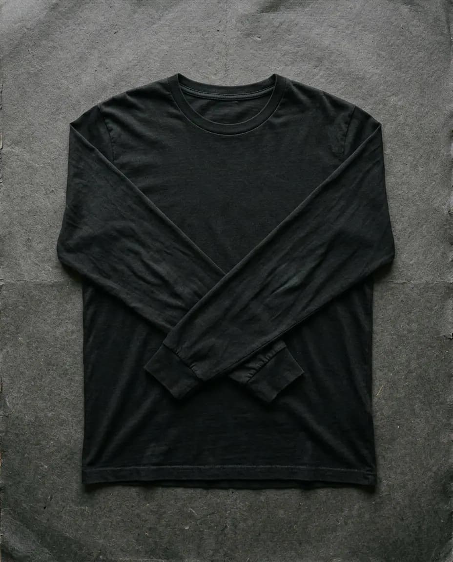 Remera negra de manga larga con las mangas cruzadas sobre un fondo de papel oscuro