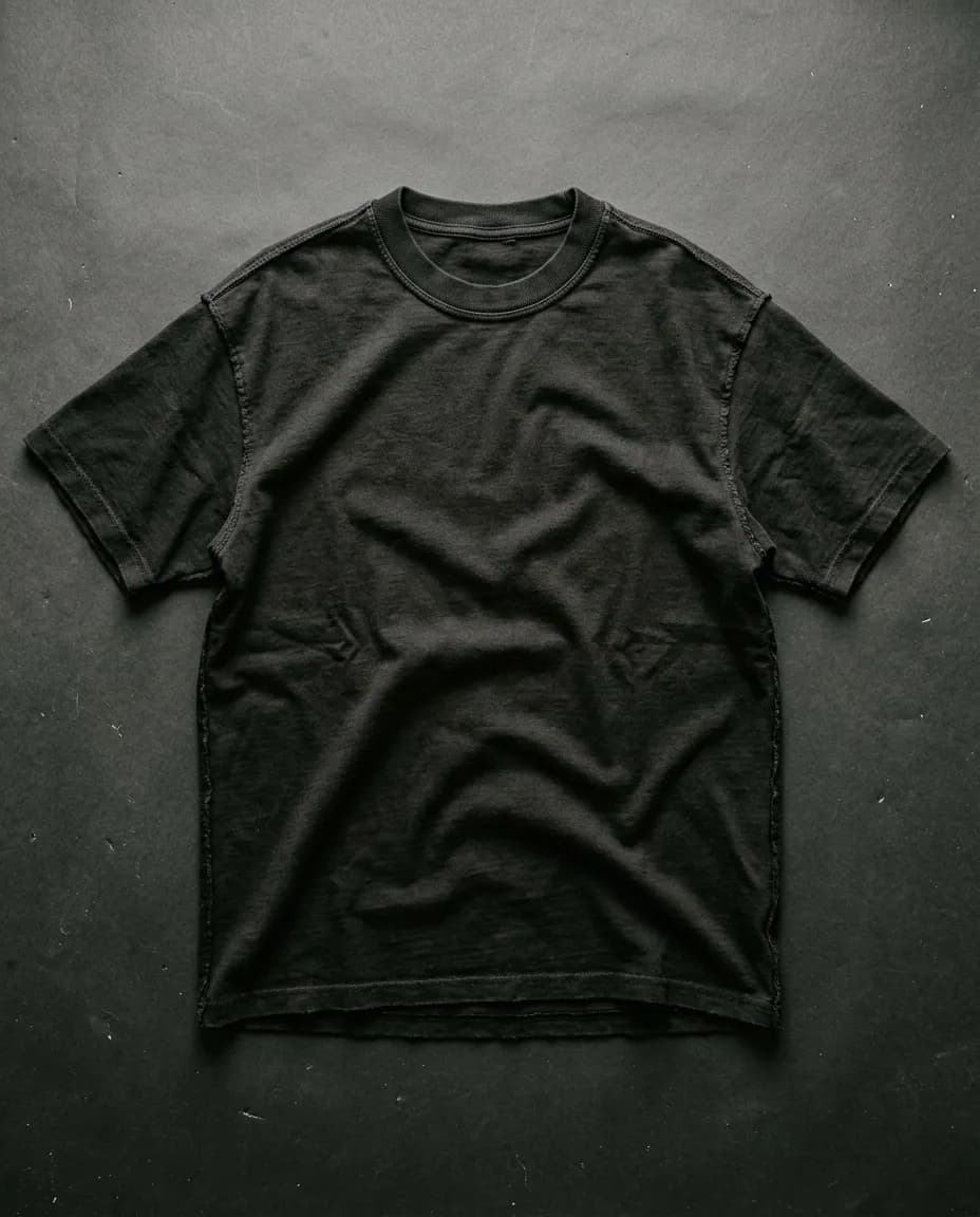 Remera oversize de algodón negro apoyada sobre un fondo de papel oscuro