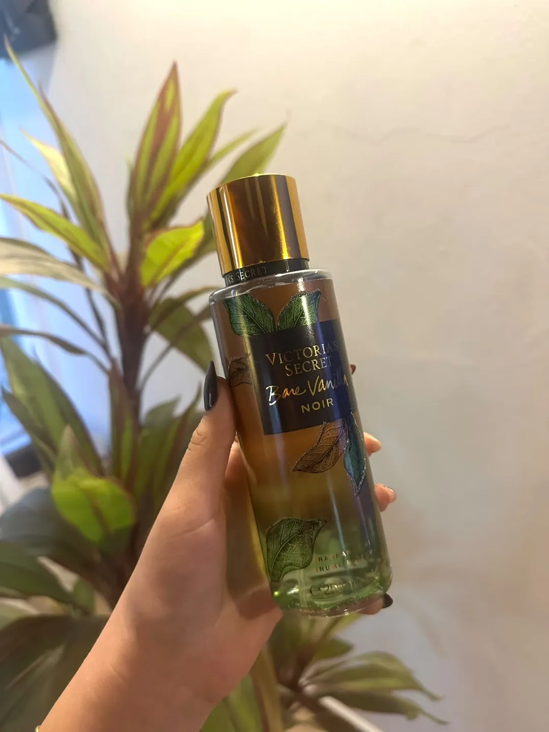 Frasco de body splash Victoria’s Secret Bare Vanilla Noir, con etiqueta negra y hojas doradas, sostenido en la mano
