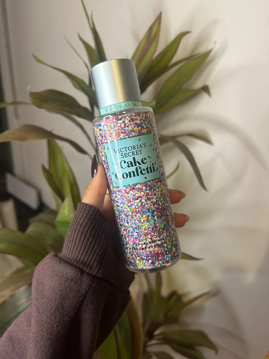 Frasco de body splash Victoria’s Secret Cake Confetti, cubierto de confeti de colores, sostenido en la mano